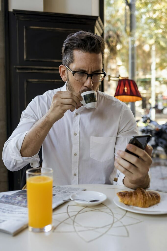 Businessman having breakfast in a cafe and checking cell phone